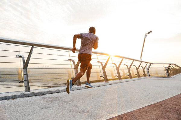 Side view of a young african man jogger exercising outdoors on a bridge