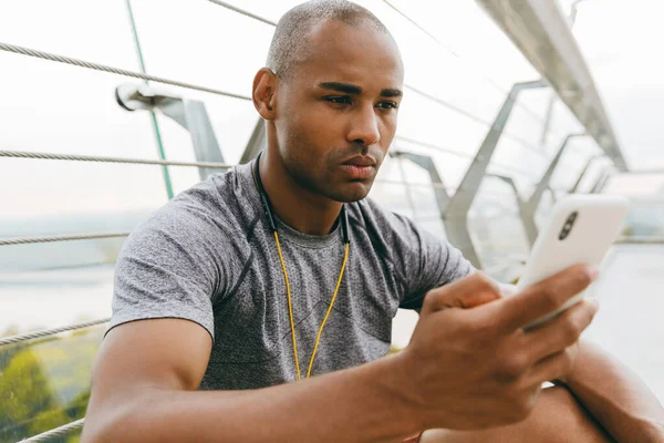 Desportivo Jovem Africano Digitando Telefone Inteligente Enquanto Descansa Livre Ponte — Fotografia de Stock