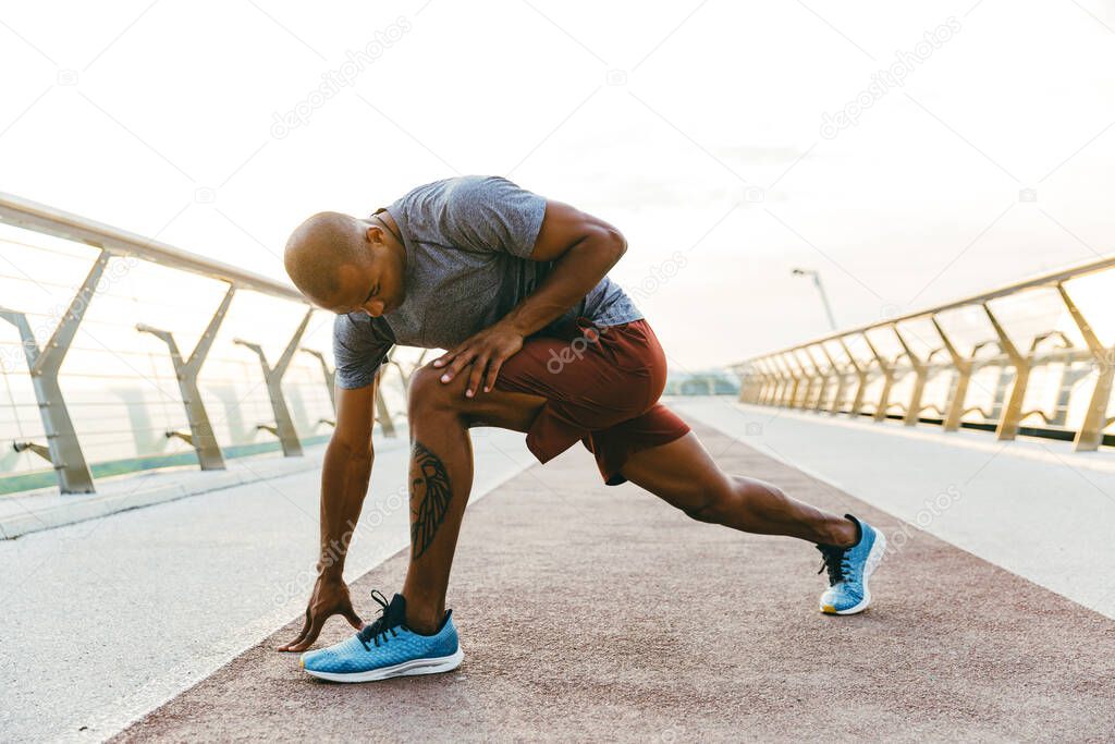 Relaxed african sportsman stretching while standing on the bridge