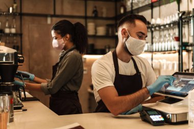 İçeride karantina sırasında resepsiyonda kahve servisi yapan tıbbi maske takan iki barmen.
