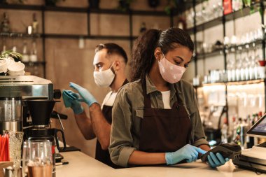İçeride karantina sırasında resepsiyonda kahve servisi yapan tıbbi maske takan iki barmen.