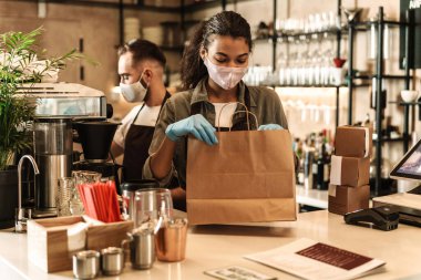 İçeride karantina sırasında resepsiyonda kahve servisi yapan tıbbi maske takan iki barmen.