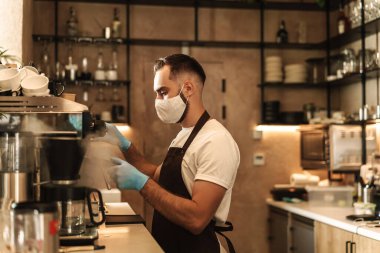 Barista virüs için koruyucu bir maske takıyor, tek kullanımlık bardaklarda kahve hazırlıyor ve servis ediyor.