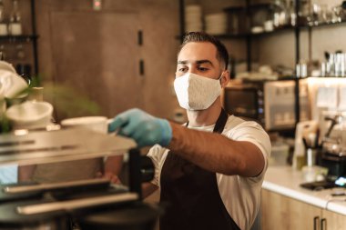 Barista virüs için koruyucu bir maske takıyor, tek kullanımlık bardaklarda kahve hazırlıyor ve servis ediyor.