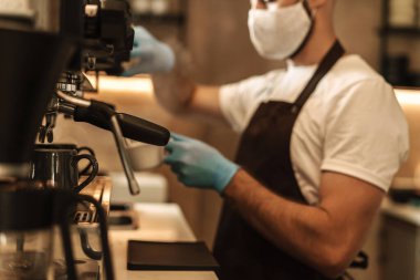 Barista virüs için koruyucu bir maske takıyor, tek kullanımlık bardaklarda kahve hazırlıyor ve servis ediyor.