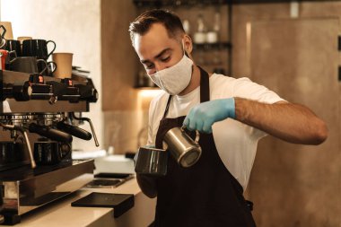 Barista virüs için koruyucu bir maske takıyor, tek kullanımlık bardaklarda kahve hazırlıyor ve servis ediyor.