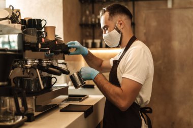 Barista virüs için koruyucu bir maske takıyor, tek kullanımlık bardaklarda kahve hazırlıyor ve servis ediyor.