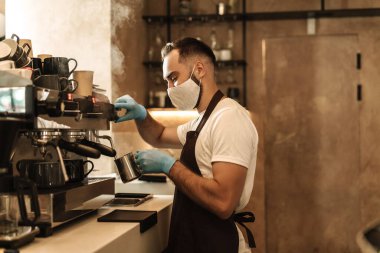 Barista virüs için koruyucu bir maske takıyor, tek kullanımlık bardaklarda kahve hazırlıyor ve servis ediyor.