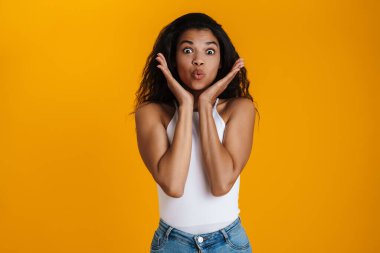 Çekici, mutlu, sıradan kıyafetler giyen Afrikalı bir kadın sarı arka planda tek başına duruyor.