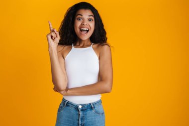 Heyecanlı genç Afrikalı kadın parmağıyla işaret ediyor, sarı üzerinde izole edilmiş bir fikri var.