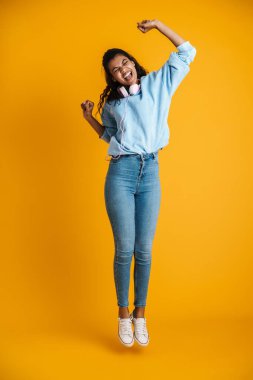 Sarı duvardan izole edilmiş, kulaklıklı heyecanlı Afrikalı Amerikalı kadının görüntüsü.