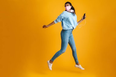 Sarı duvarın üzerinden atlarken cep telefonu ve kulaklık takan Afro-Amerikan kadın görüntüsü