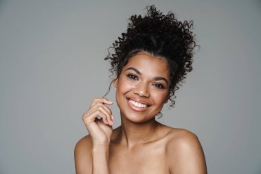 Gri duvardan izole edilmiş kameraya bakıp gülümseyen Afro-Amerikan kadın resmi.