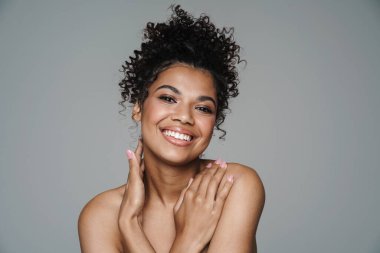 Gri duvardan izole edilmiş kameraya bakıp gülümseyen Afro-Amerikan kadın resmi.