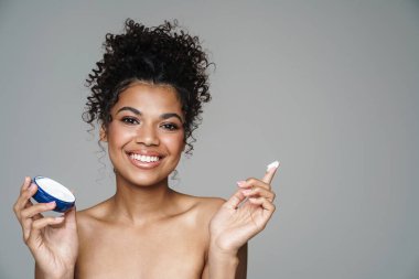 Gri duvardan izole edilmiş yüz kremi süren Afro-Amerikan kadın resmi