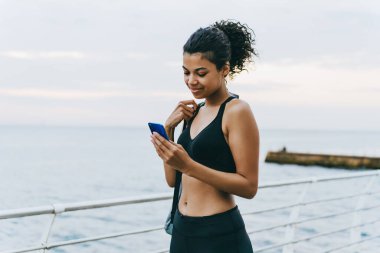 Gezintide yürürken cep telefonu kullanan Afro-Amerikan sporcu kadının resmi