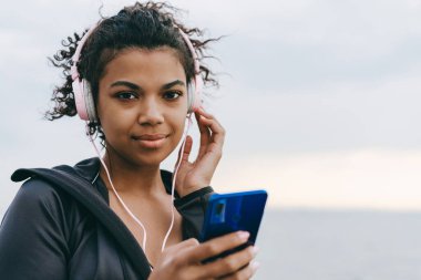 Gezintide yürürken cep telefonu ve kulaklık kullanan memnun bir Afrikalı Amerikalı kadın görüntüsü