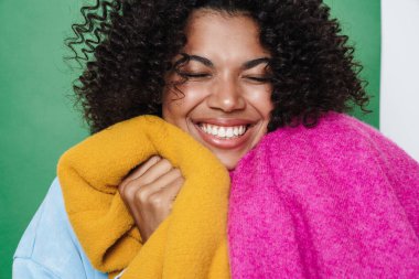 Çok renkli arka planda izole edilmiş giysileri tutarken gülümseyen Afro-Amerikan kadını.