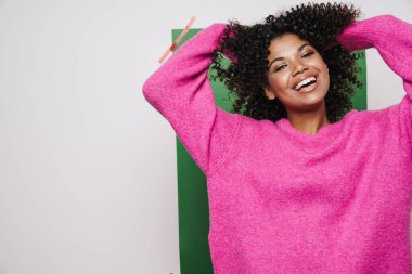 Neşeli Afro-Amerikan kadın görüntüsü. Gülümseyen ve saçlarıyla dalga geçen. Renkli arka planda izole edilmiş.