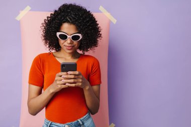 Çok renkli arka planda izole edilmiş cep telefonu kullanan ciddi Afrikalı Amerikalı kadın görüntüsü
