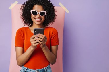 Çok renkli arka planda cep telefonu kullanırken gülümseyen mutlu Afrikalı Amerikalı kadın görüntüsü
