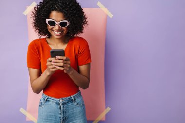 Çok renkli arka planda cep telefonu kullanırken gülümseyen mutlu Afrikalı Amerikalı kadın görüntüsü