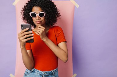 Çok renkli arka planda izole edilmiş cep telefonu kullanan ciddi Afrikalı Amerikalı kadın görüntüsü