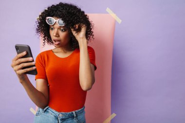 Çok renkli arka planda izole edilmiş cep telefonu kullanan şaşırmış Afrikalı Amerikalı kadın görüntüsü