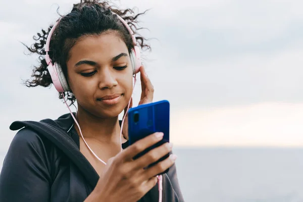 Imagen Una Mujer Afroamericana Complacida Usando Teléfono Celular Auriculares Mientras —  Fotos de Stock