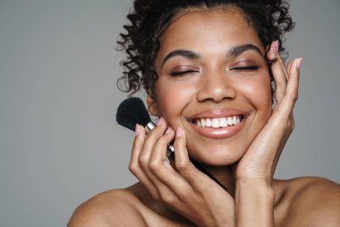 Gri duvarın üzerinde toz fırçası tutan ve gülümseyen üstsüz Afro-Amerikan kadın resmi