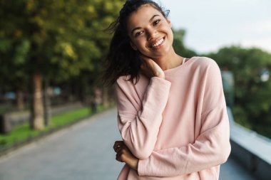 Mutlu Afrikalı Amerikalı bir kızın yaz parkında yürürken gülümsemesi.