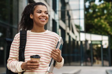 Keyifli Afro-Amerikan kız görüntüsü. Şehir caddesinde dizüstü bilgisayarla yürürken kahve içiyor.