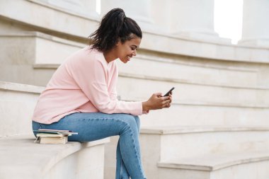 Merdivenlerde otururken cep telefonu kullanan Afrikalı Amerikalı öğrenci görüntüsü