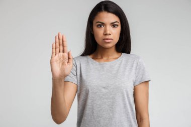 Ciddi bir Afrikalı genç kadının portresi. Gri arka planda avuçlarında izole bir şekilde dur işareti yapıyor.