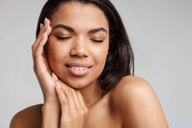 Gri arka planda yalnız poz veren güzel, genç, şehvetli, üstsüz bir Afrikalı kadının portresi.