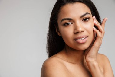 Gri arka planda yalnız poz veren güzel, genç, şehvetli, üstsüz bir Afrikalı kadının portresi.