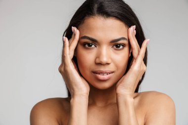 Gri arka planda yalnız poz veren güzel, genç, şehvetli, üstsüz bir Afrikalı kadının portresi.