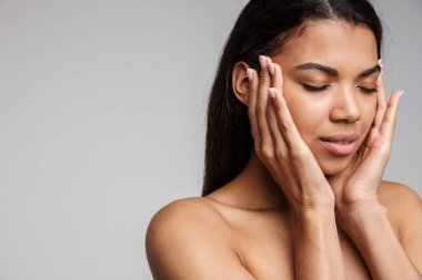 Gri arka planda yalnız poz veren güzel, genç, şehvetli, üstsüz bir Afrikalı kadının portresi.