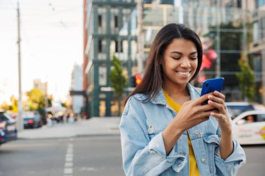 Genç gülümseyen Afrikalı kadın sokakta cep telefonu kullanıyor.