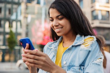 Genç gülümseyen Afrikalı kadın sokakta cep telefonu kullanıyor.