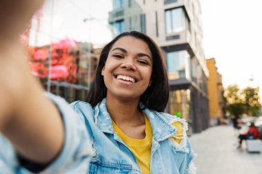 Neşeli Afro-Amerikan kadın görüntüsü. Gülümseyen ve şehirde yürürken selfie çeken.
