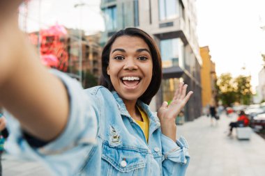 Neşeli Afro-Amerikan kadın görüntüsü. Gülümseyen ve şehirde yürürken selfie çeken.