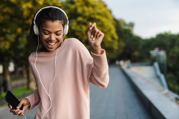 Imagen Una Niña Afroamericana Sonriente Usando Teléfono Móvil Auriculares Mientras —  Fotos de Stock