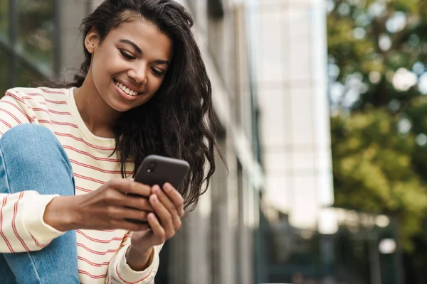 Immagine Una Sorridente Ragazza Afroamericana Che Usa Cellulare Mentre Seduta — Foto Stock