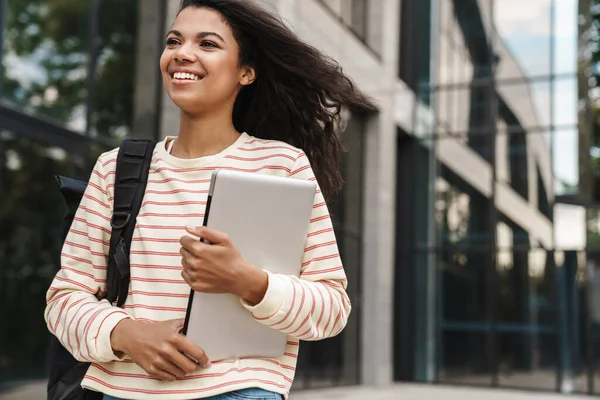 街を歩きながらノートパソコンを持っているアフリカ系アメリカ人の女の子の笑顔のイメージ — ストック写真