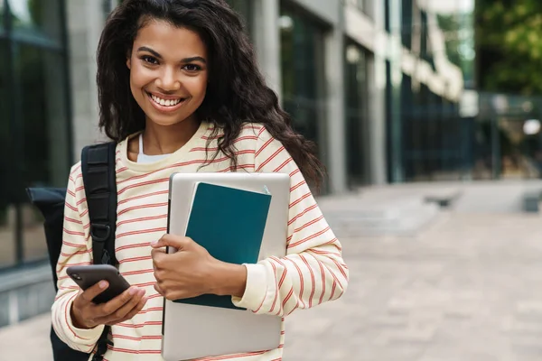 街中でノートパソコンを持ちながら歩く陽気なアフリカ系アメリカ人の女の子のイメージ — ストック写真