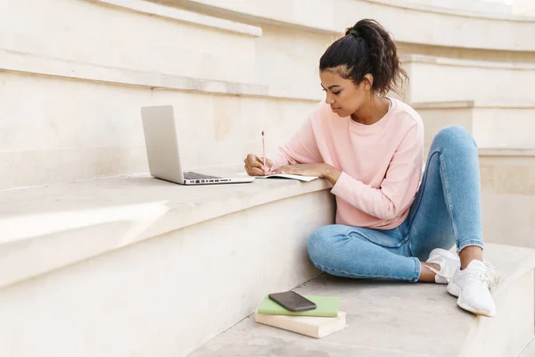 Imagen Una Estudiante Afroamericana Complacida Haciendo Tarea Con Portátil Mientras —  Fotos de Stock