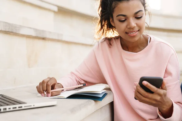 Imagen Una Estudiante Afroamericana Complacida Haciendo Tarea Con Portátil Mientras —  Fotos de Stock