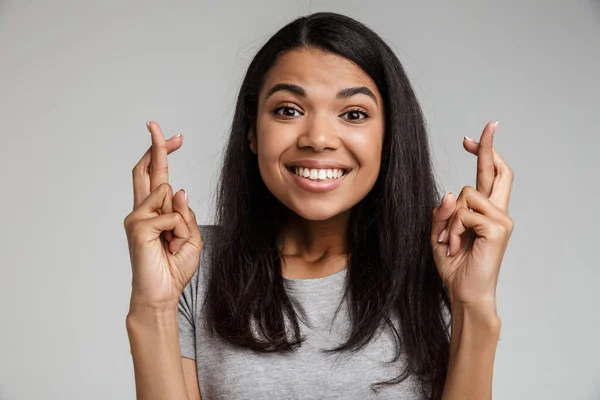 Beautiful african woman with fingers crossed isolated on gray, wishing good luck