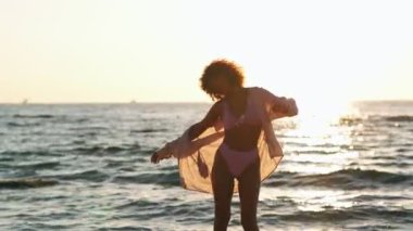 Mayolu genç Afrikalı bir kadın sahilde dans ediyor.